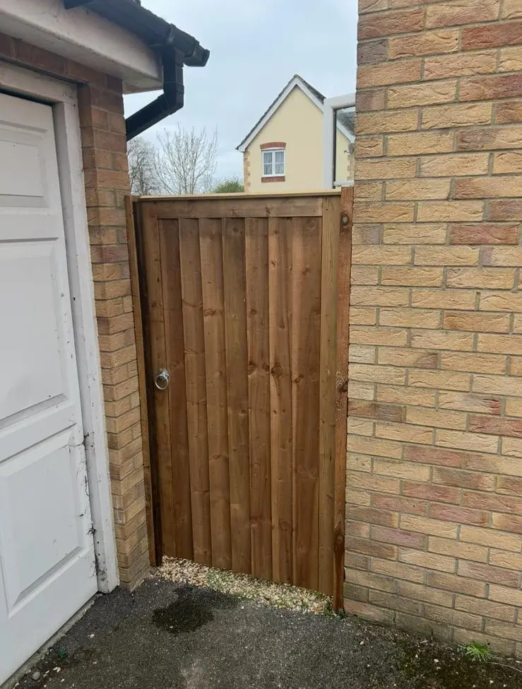 Straight-top timber gate installed between a garage wall and brick boundary with a secure metal latch